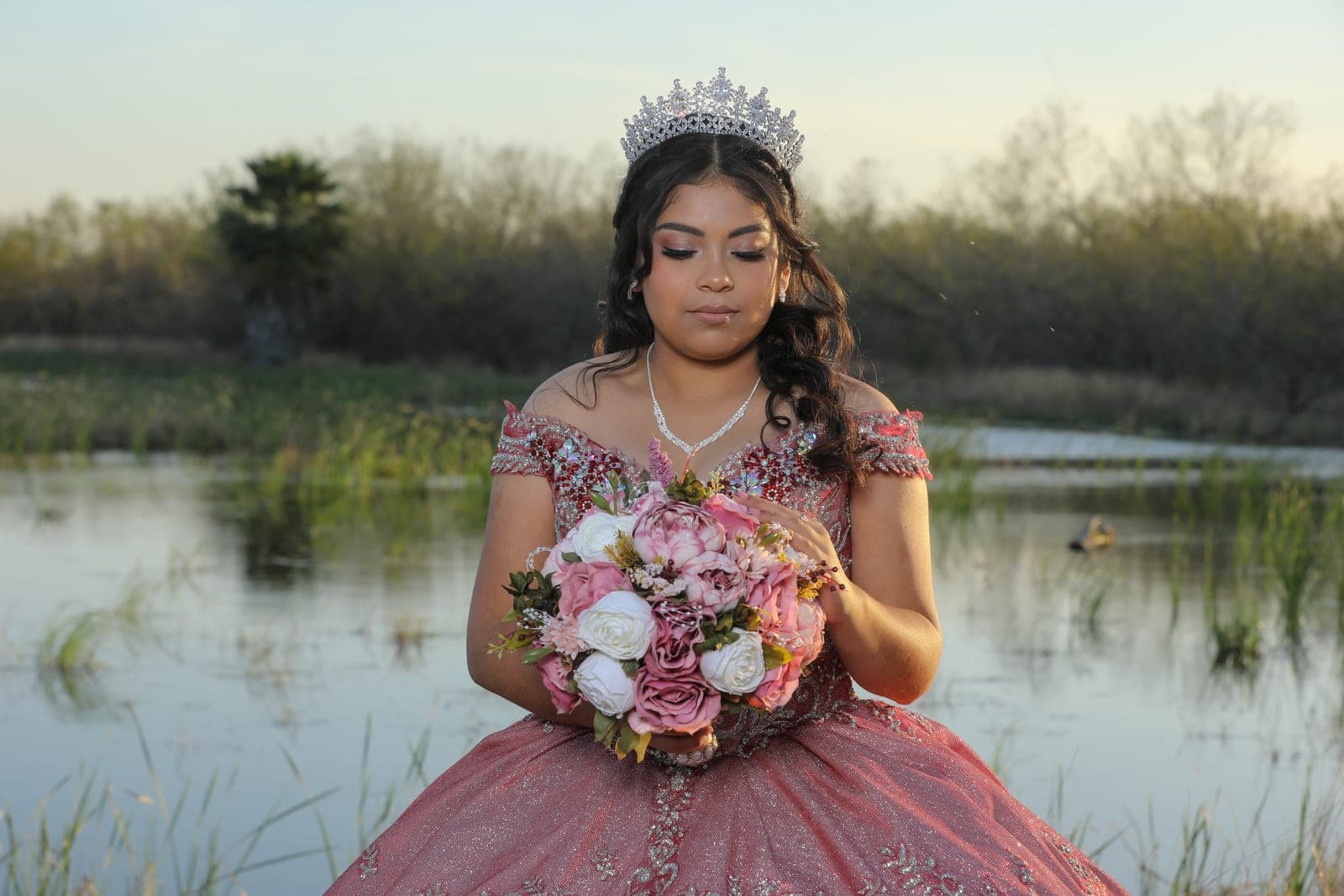 Quinceañera in a rose ball gown at golden hour by the water