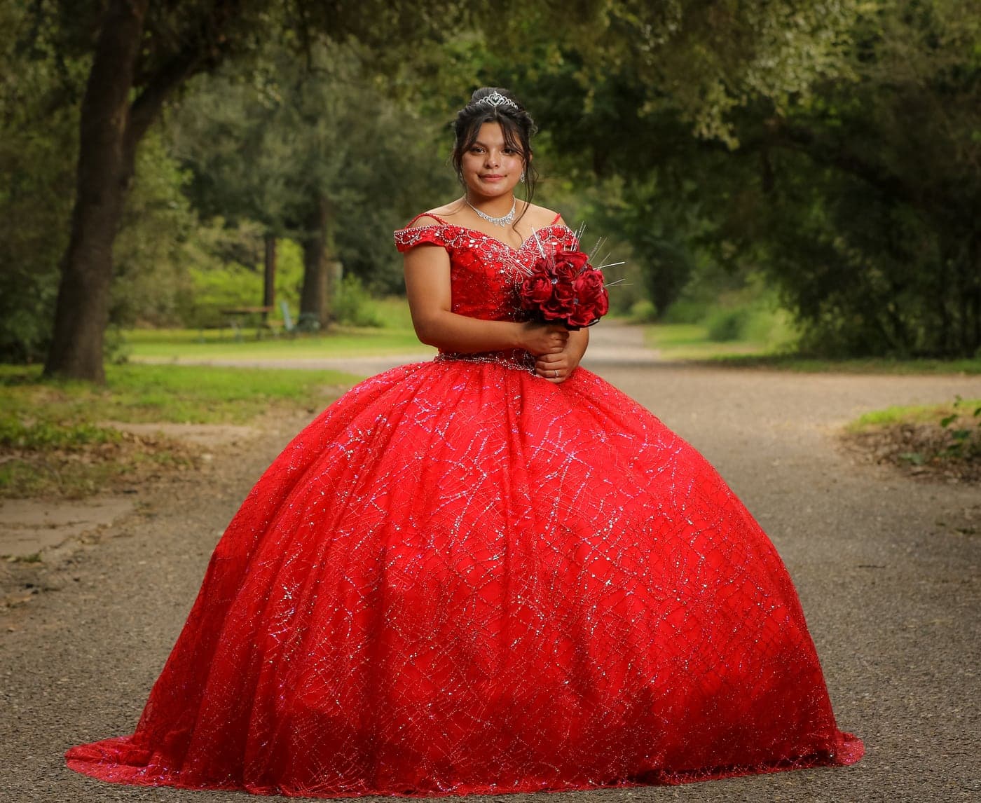 Quinceañera in a red ball gown on a tree-lined path