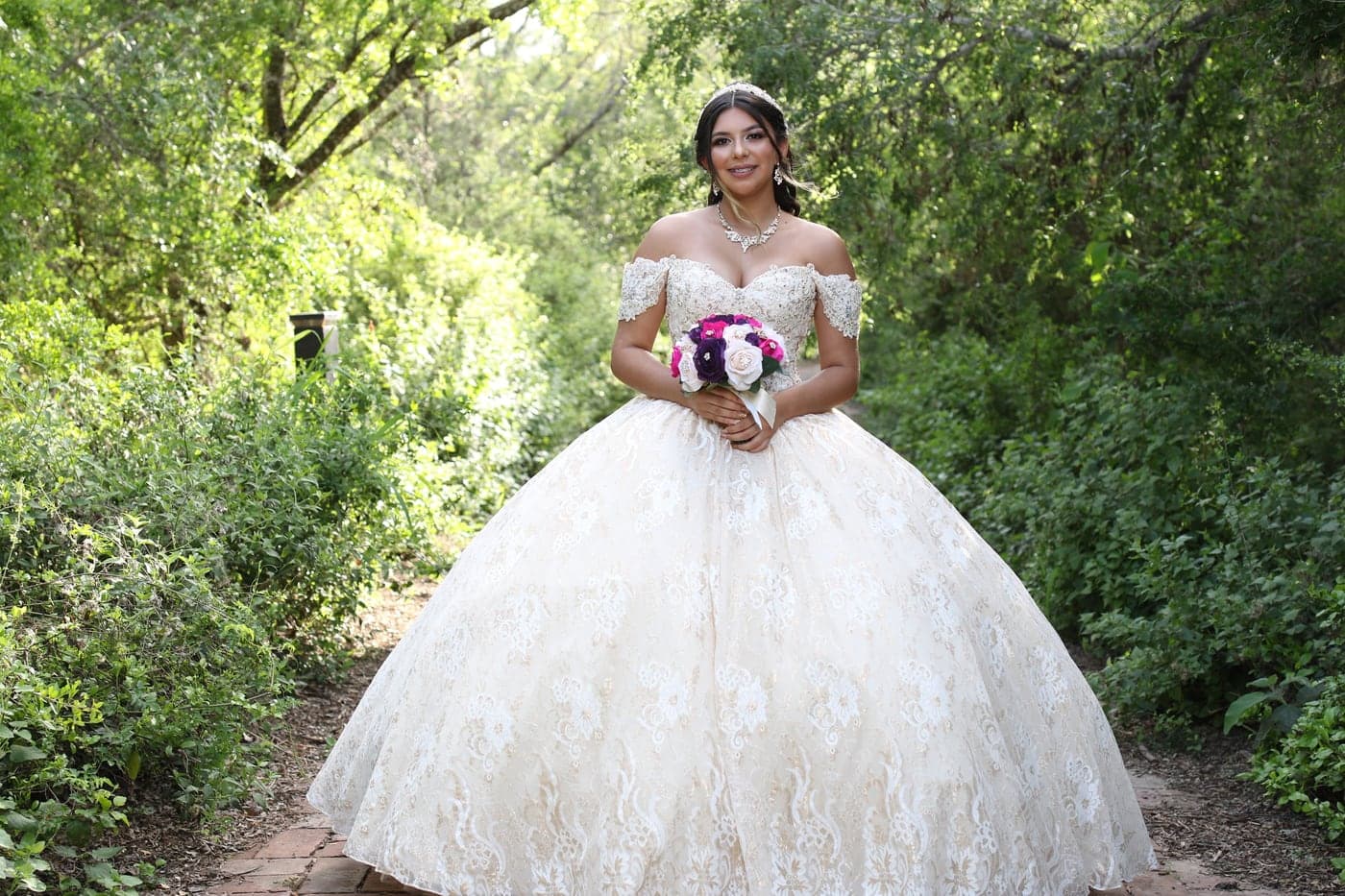 Quinceañera in an ivory ball gown holding her bouquet in a garden