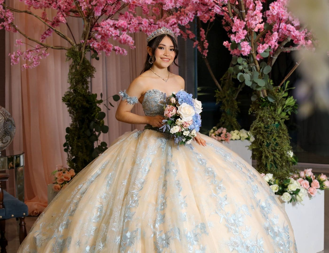 Quinceañera in a champagne gown beneath blooming cherry blossoms