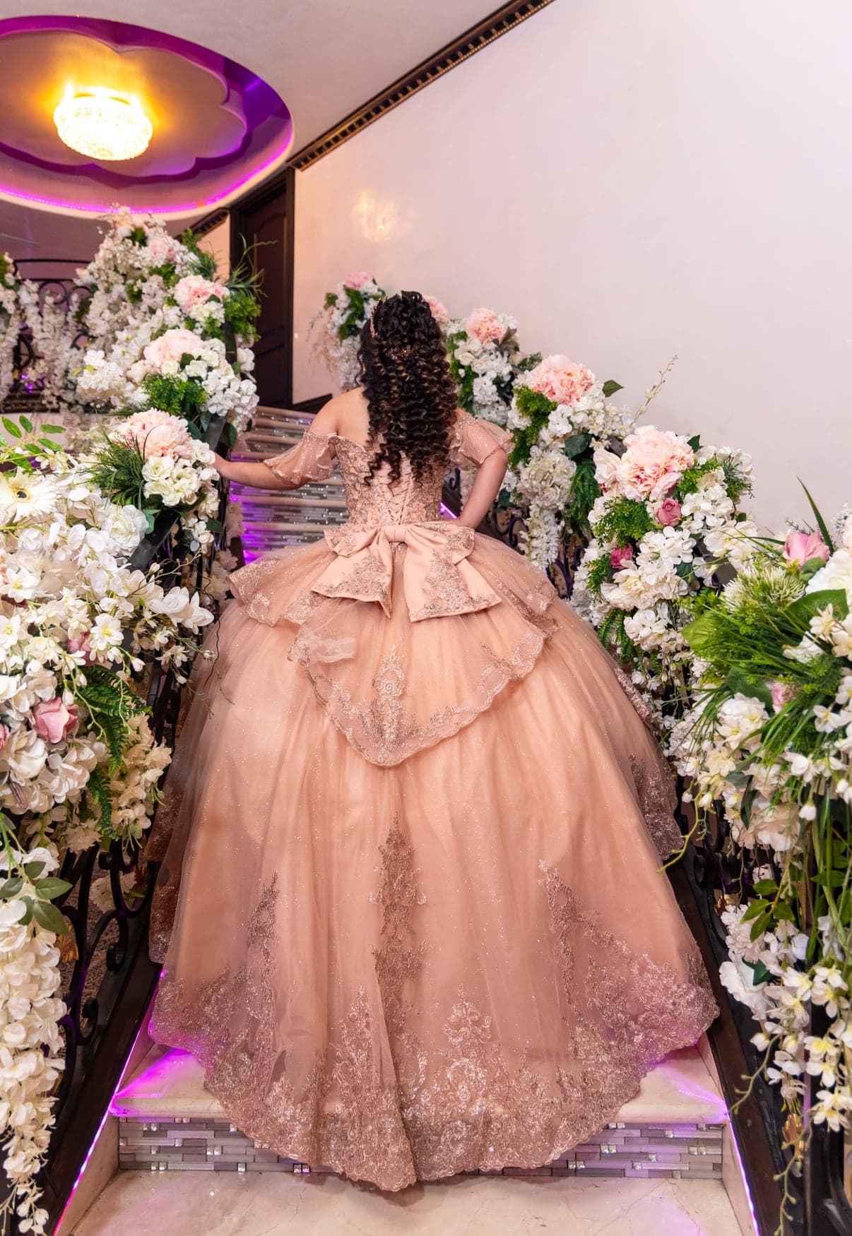 Quinceañera in a rose gown with a full train among florals
