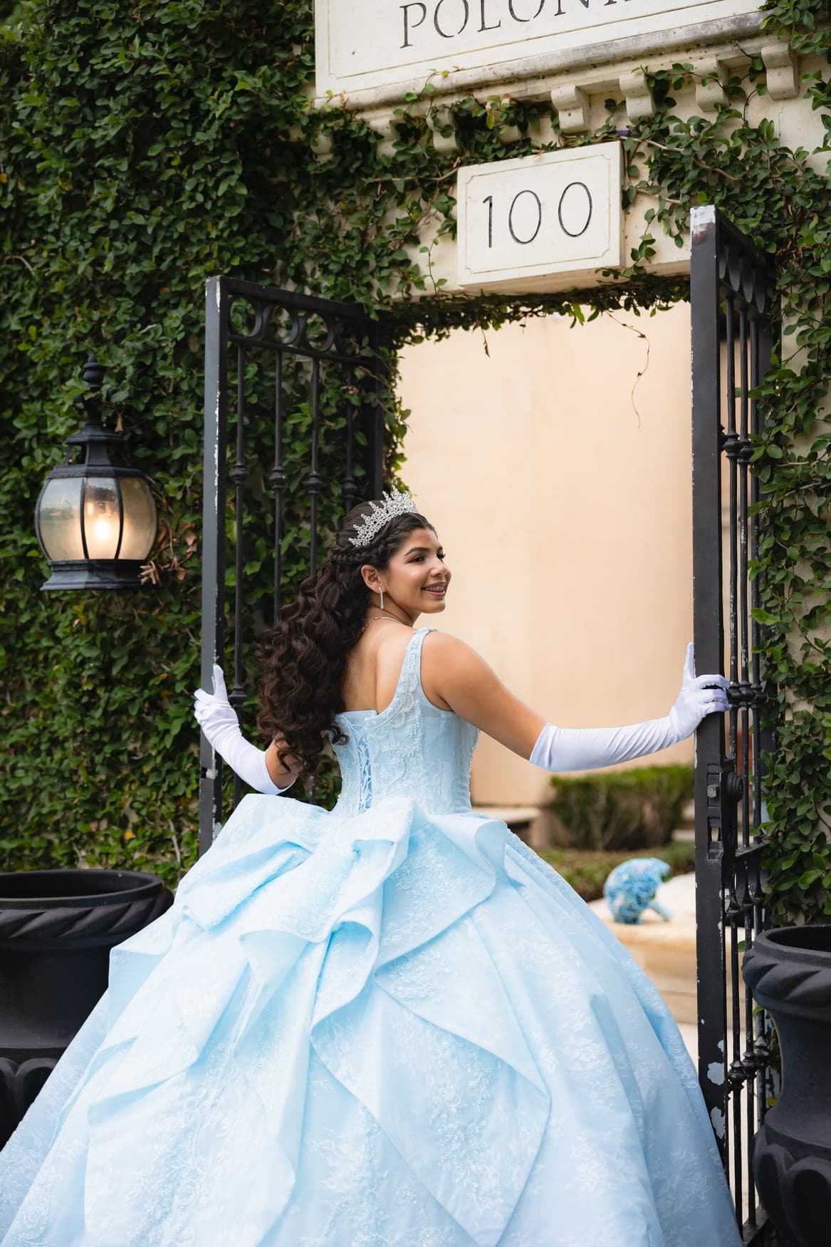 Quinceañera in a light-blue gown and gloves by an ivy wall