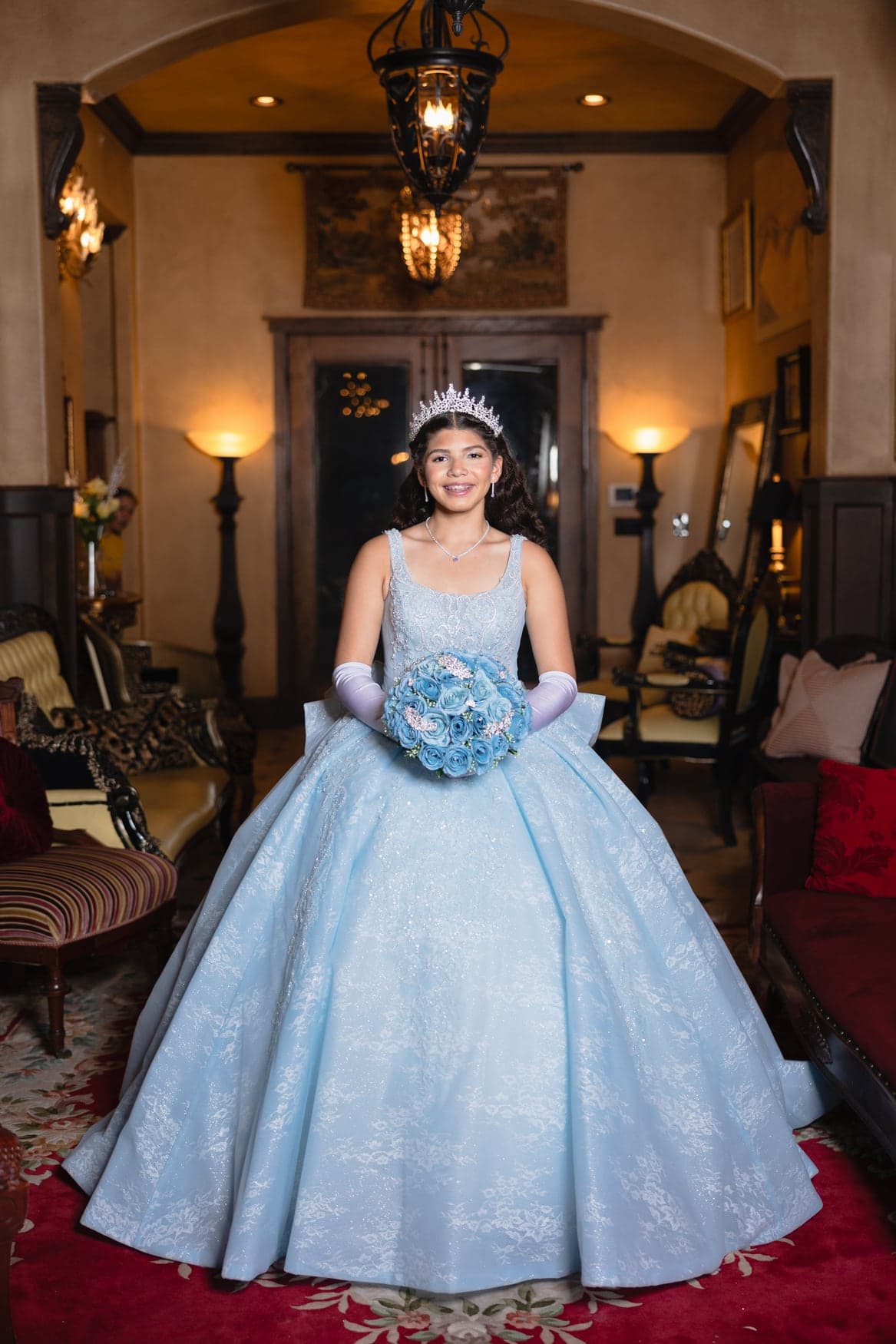 Quinceañera in a light-blue gown and tiara in an elegant interior