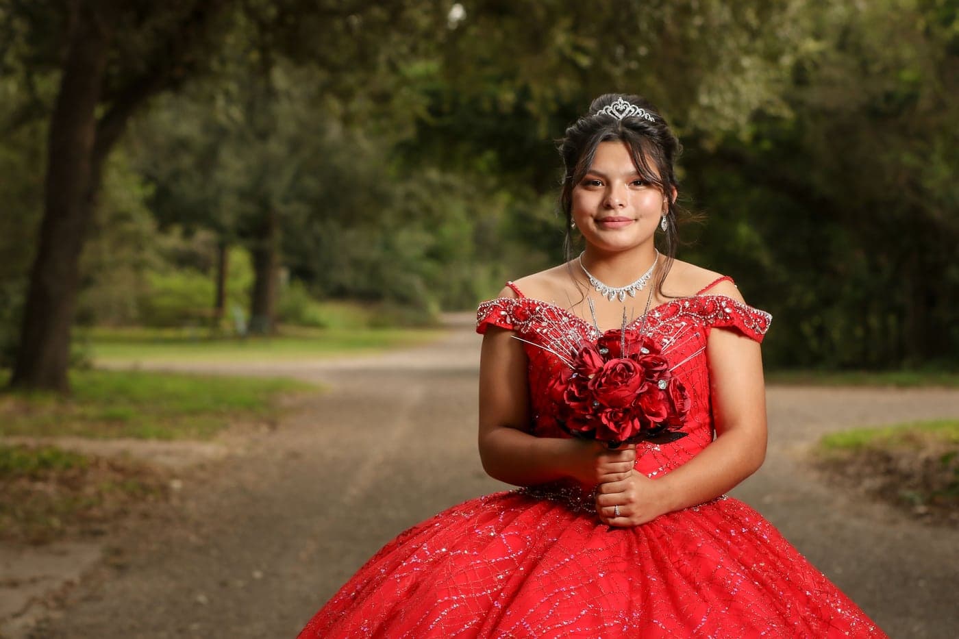Quinceañera in a red sparkling ball gown on a garden path