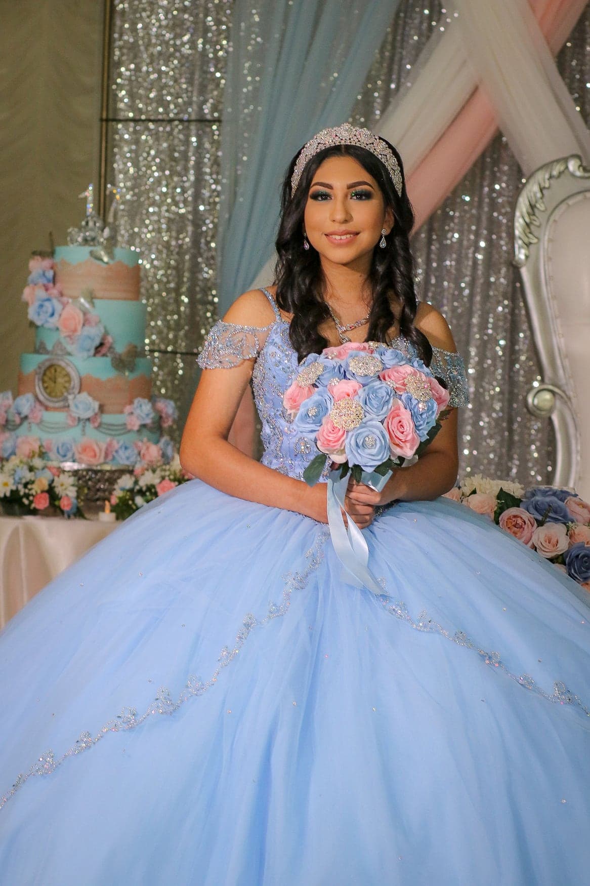 Quinceañera in a light-blue floral gown beside her cake